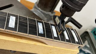 5弦ベースの指板にフレットプレスでフレットを埋め込んでいるところ