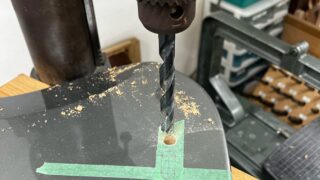 ボール盤で5弦ベースのボディのバック面に弦止めブッシュの穴を開けているところ