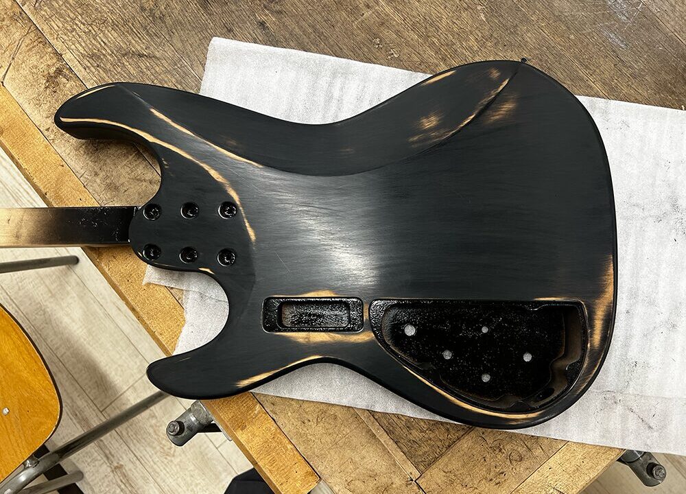 5弦ベースのボディに塗った黒の着色をサンディングペーパーで磨いているところ