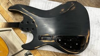 5弦ベースのボディに塗った黒の着色をサンディングペーパーで磨いているところ