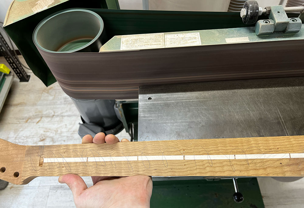 ギターのネックの指板接着面をエコノミーサンダーで削って平面にしているところ