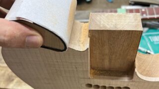 シンラインタイプのギターのボディのホーン部分のくびれをサンドペーパーで磨いているところ