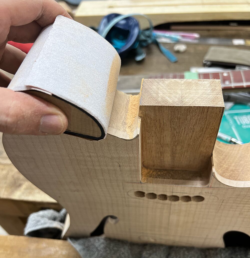 シンラインタイプのギターのボディのホーン部分のくびれをサンドペーパーで磨いているところ