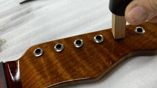 ギターヘッドにクルーソンペグのブッシュを玄能で叩いて埋め込んでいるところ